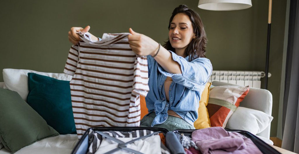 Des mains féminines plient des vêtements amples en coton clair dans un tiroir de commode, sans visage visible